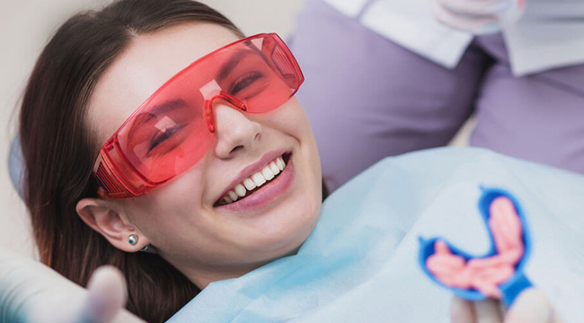 Young girl wearing red protective eyewear smiling in dental chair during examination.