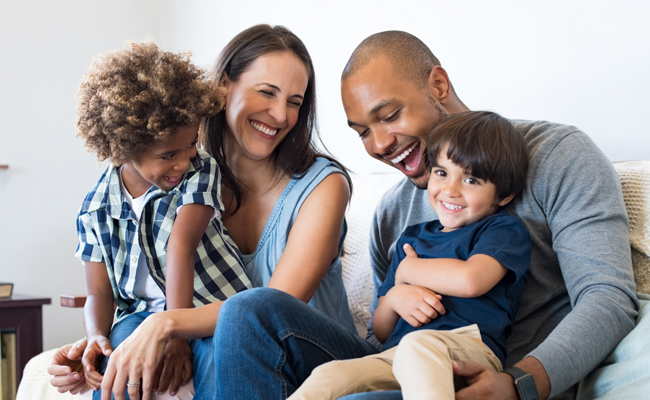 Happy family of four smiling together indoors in casual clothing.