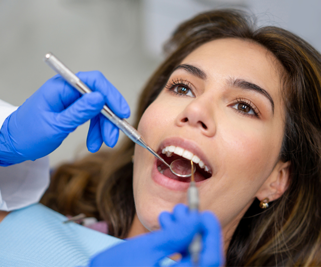 Woman receiving dental examination from dentist wearing blue gloves in clinical setting.
