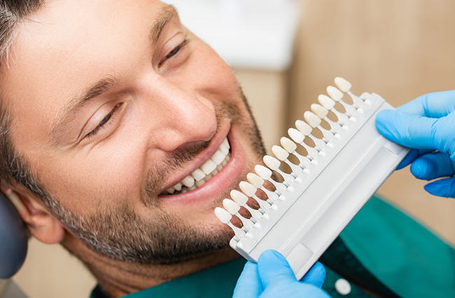 Man smiling while dentist shows tooth shade guide during dental consultation at office.