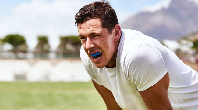 Man in white shirt smiling outdoors on grass field during daytime.