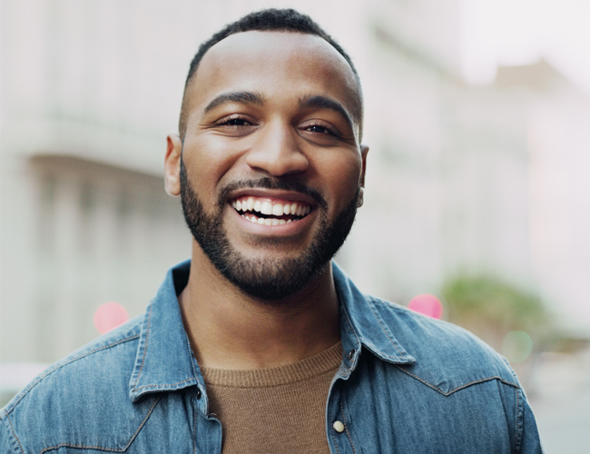 Smiling man in denim shirt outdoors, professional headshot for dental practice website.