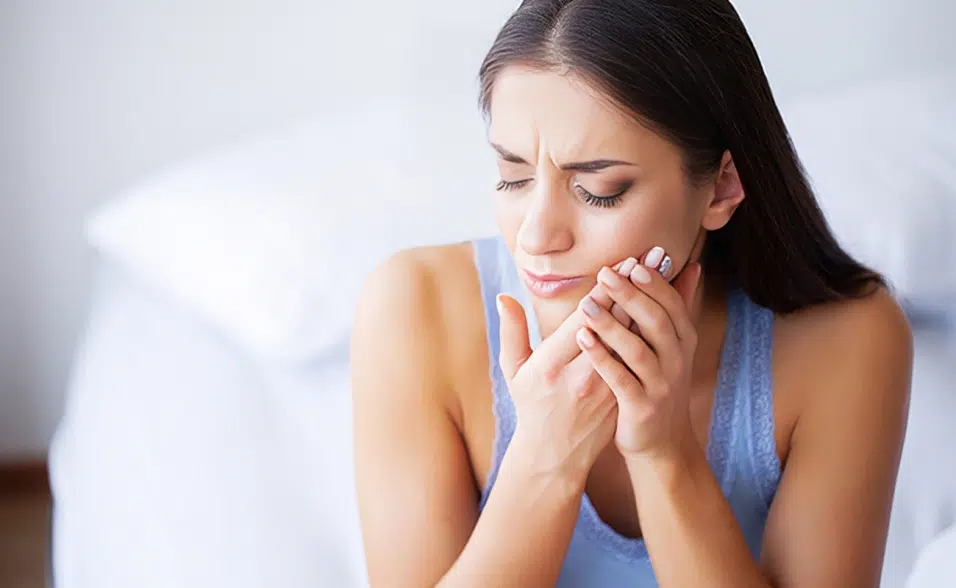 Woman holding jaw in pain, appearing distressed, with blurred background suggesting dental discomfort.