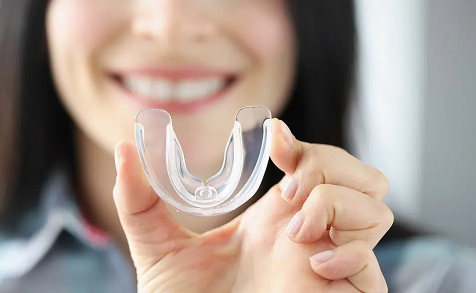 Woman smiling while holding clear dental aligner tray in front of her face.