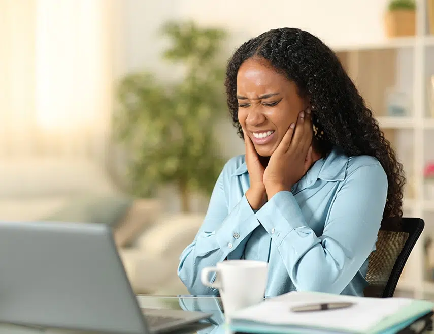 Woman in blue shirt smiling at laptop with coffee cup at desk in office.