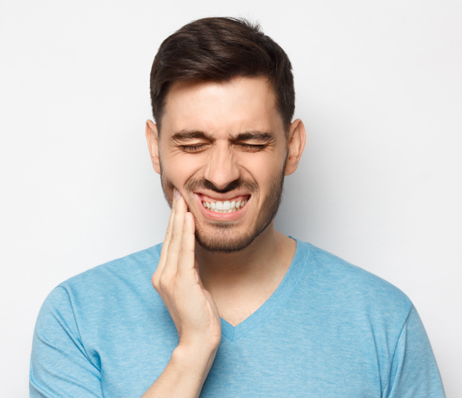 Man in blue shirt touching face with hand, smiling against white background, dental clinic setting.