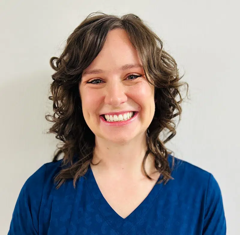 Smiling woman with curly brown hair wearing blue shirt against white background.