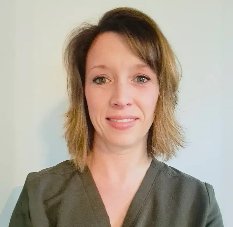 Woman in olive green scrubs smiling at camera, professional headshot for dental practice.