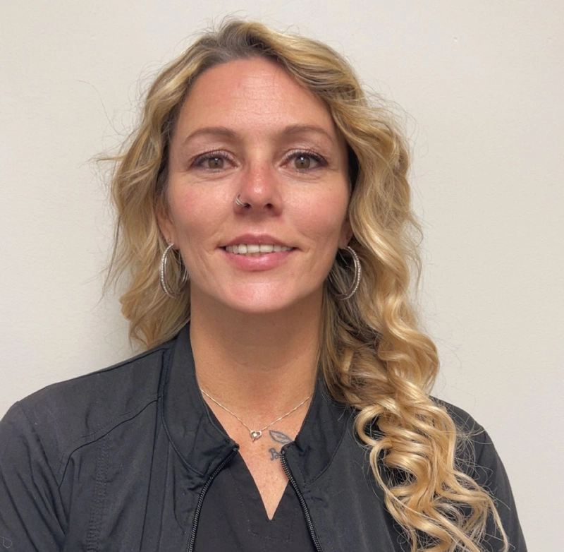 Professional headshot of a woman with wavy blonde hair wearing a dark shirt against a neutral background.